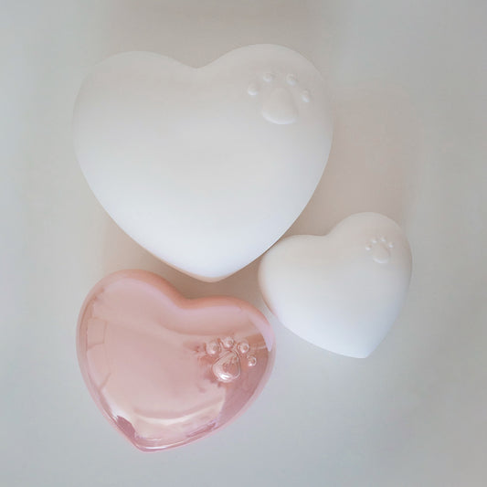 Beautiful ceramic heart urn in pink, white, navy blue. Embossed with raised paw print design. Unique urn for display on white stand personaled with pet name and message. They left a paw print on your heart
