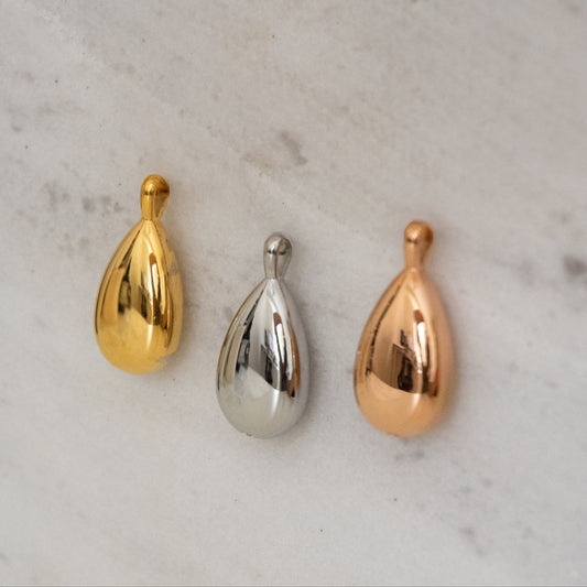 Three metallic teardrop-shaped objects in gold, silver, and rose gold on a marble surface.