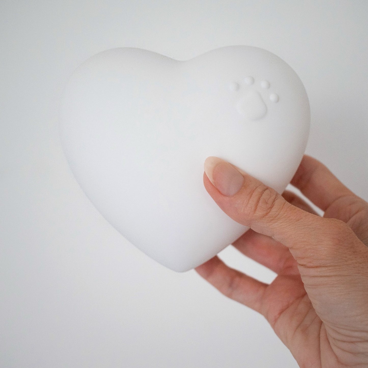 Beautiful ceramic heart urn in pink, white, navy blue. Embossed with raised paw print design. Unique urn for display on white stand personaled with pet name and message. They left a paw print on your heart