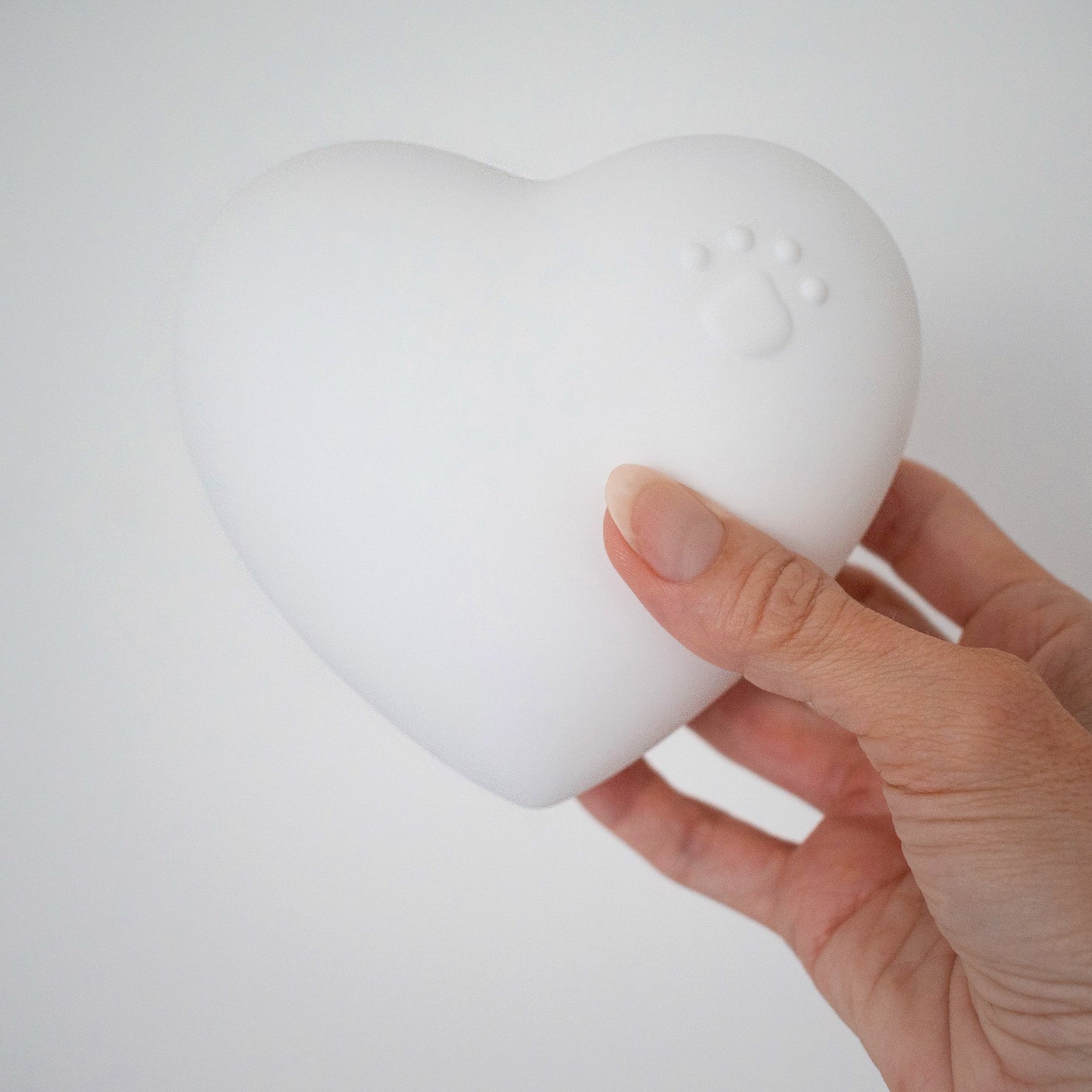 Beautiful ceramic heart urn in pink, white, navy blue. Embossed with raised paw print design. Unique urn for display on white stand personaled with pet name and message. They left a paw print on your heart