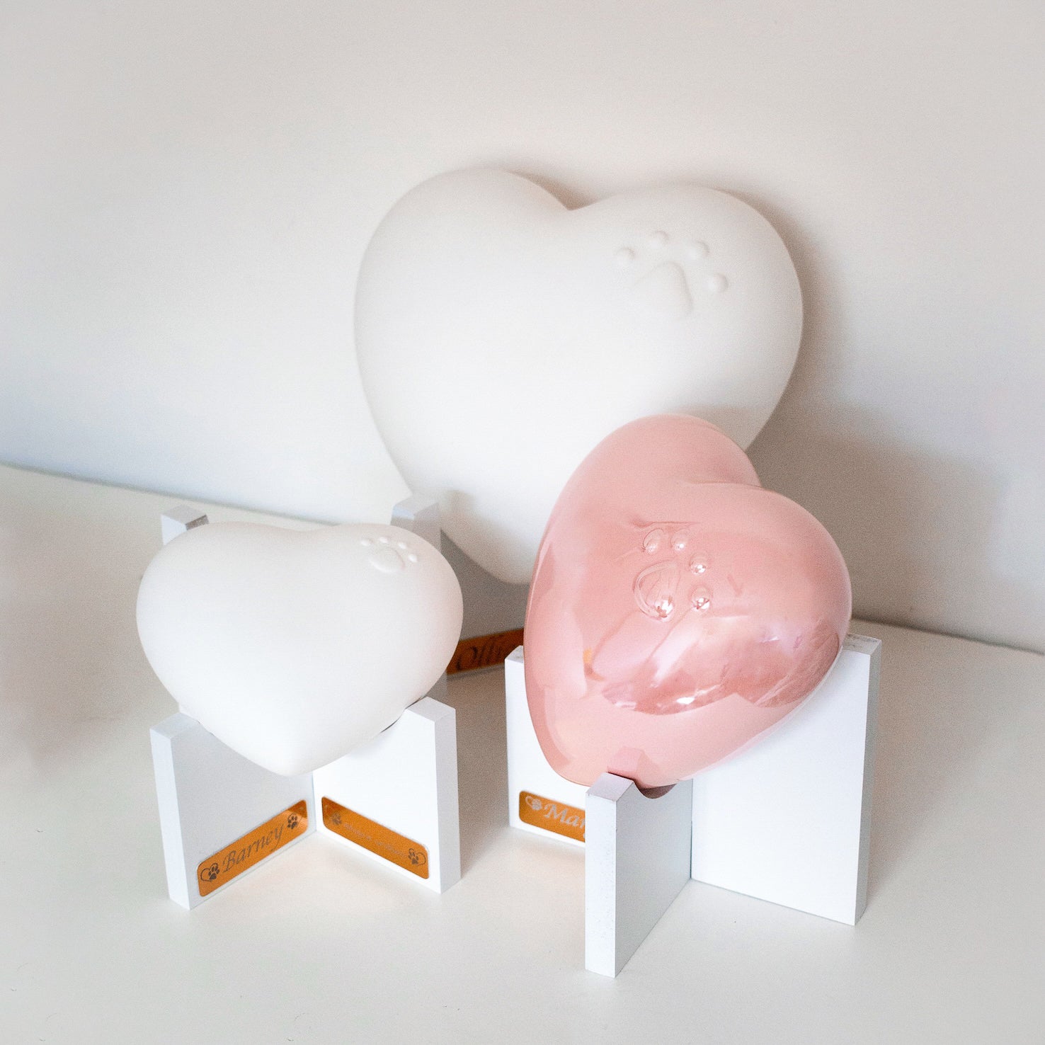 Beautiful ceramic heart urn in pink, white, navy blue. Embossed with raised paw print design. Unique urn for display on white stand personaled with pet name and message. They left a paw print on your heart